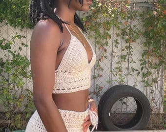 May include: A woman wearing a white crochet top and matching shorts. The top is a halter style with a V-neckline. The shorts have a drawstring waist.