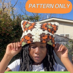 Könnte beinhalten: Gehäkelte Katzenohren-Mütze im Granny-Square-Muster. Die Mütze hat Quadrate in Braun, Orange, Weiß und Grün. Der Text "PATTERN ONLY" befindet sich in einem orangefarbenen Oval. Der Text "PLEASE TAG @VIRGOSTARRSTUDIOS" ist unten.