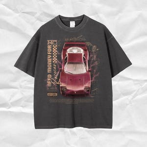Könnte beinhalten: Ein schwarzes T-Shirt mit einem grafischen Druck eines roten Sportwagens. Der Text "Need Money For Racecar" ist auf dem Shirt gedruckt. Das Shirt hat ein Warnhinweis für Eltern.