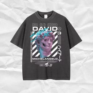May include: A black t-shirt with a graphic print of a bust sculpture with the text "DAVID" and "MICHELANGELO" in white and blue. The graphic also includes a smiley face and a globe.