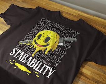 Könnte beinhalten: Schwarzes T-Shirt mit einem gelben Smiley-Grafik, das schmilzt und ein Messer durchstoßen hat. Der Text "STABILITY" wird mehrmals in Weiß wiederholt.