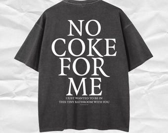 以下が含まれることがあります： 「NO COKE FOR ME」の白い文字がプリントされた濃いグレーのTシャツ。下には「I JUST WANTED TO BE IN THIS TINY BATHROOM WITH YOU」と書かれています。半袖でゆったりとしたフィット感です。