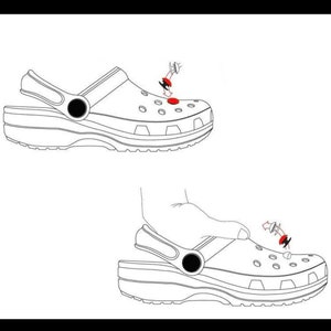 May include: A white clog with a black strap and a red button. The button is being pressed down with a finger. The clog is shown from the side.
