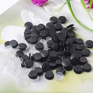 May include: A pile of black plastic snap buttons with a few clear plastic snap buttons. The buttons are round and have a small hole in the center.