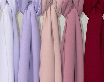 May include: Five different colored scarves hanging on a white background. The scarves are white, lavender, light pink, pink, and burgundy.