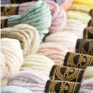 Peut inclure: Gros plan sur une vari&eacute;t&eacute; de bobines de fil &agrave; broder DMC dans des couleurs pastel, notamment bleu clair, lavande, vert p&acirc;le, beige et cr&egrave;me. Les bobines sont dispos&eacute;es en rang&eacute;e, avec le logo et la marque DMC visibles sur chaque bobine.