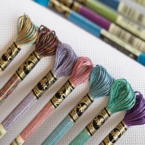 May include: Assortment of DMC embroidery floss spools in various colours, including teal, lavender, pink, and green. Each spool features the DMC logo and the text "Mouliné" and "DMC".