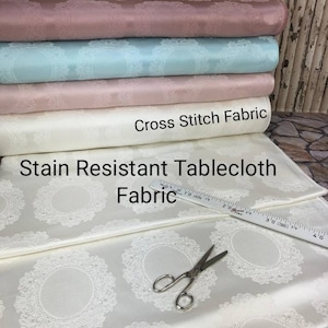May include: A close-up of a white tablecloth with a delicate lace pattern. The tablecloth is stain resistant and made of cross stitch fabric. A ruler and scissors are also visible in the image.