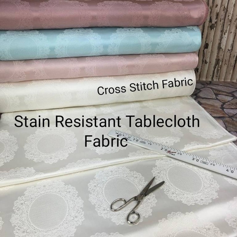 May include: A close-up of a white tablecloth with a delicate lace pattern. The tablecloth is stain resistant and made of cross stitch fabric. A ruler and scissors are also visible in the image.