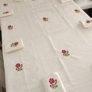 May include: White tablecloth with red embroidered roses. The tablecloth is laid out on a table with matching napkins.
