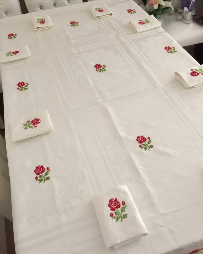 May include: White tablecloth with red embroidered roses. The tablecloth is laid out on a table with matching napkins.