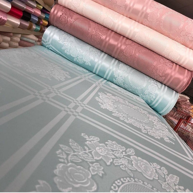 May include: Rolls of fabric in various shades of pink and blue with a white floral pattern. The fabric has a subtle sheen and a textured surface.