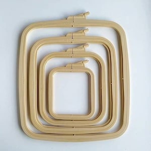 Può includere: Set di cinque cerchi da ricamo in plastica beige, con dimensioni che vanno da 10x10 cm a 20x20 cm. I cerchi sono annidati uno dentro l'altro, con il cerchio più grande in basso e il cerchio più piccolo in alto.