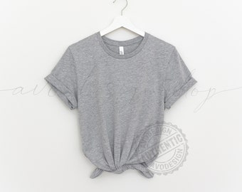 May include: A heather gray t-shirt with rolled up sleeves hanging on a white hanger against a white background. The t-shirt is knotted at the bottom.