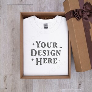 May include: A white t-shirt with the text "YOUR DESIGN HERE" printed on it, inside a brown gift box with a brown ribbon and bow.