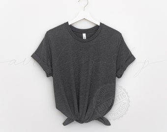 May include: A dark gray t-shirt with rolled-up sleeves hangs from a white hanger. The shirt is knotted at the waist, creating a stylish, casual look. The fabric appears soft and comfortable, perfect for everyday wear.