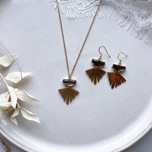 Puede incluir: Un conjunto de collar y pendientes de oro con un dise&ntilde;o de abanico geom&eacute;trico y un colgante de piedra marr&oacute;n oscuro.