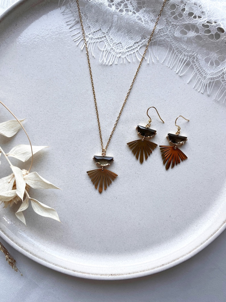 Puede incluir: Un conjunto de collar y pendientes de oro con un dise&ntilde;o de abanico geom&eacute;trico y un colgante de piedra marr&oacute;n oscuro.