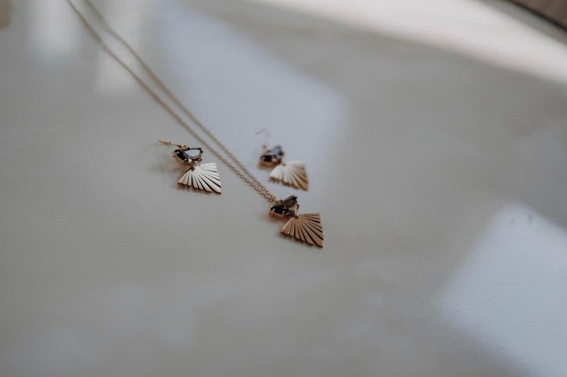 Puede incluir: Un conjunto de collar y pendientes de oro con un dise&ntilde;o de abanico geom&eacute;trico y detalles de piedras preciosas negras.