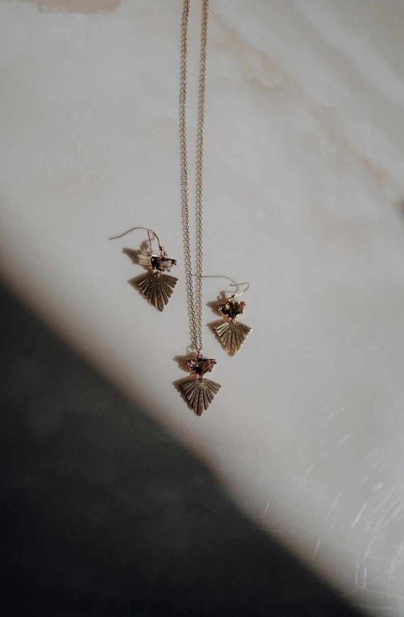 Puede incluir: Un collar y pendientes a juego de oro con un dise&ntilde;o geom&eacute;trico en forma de abanico y un acento de cristal transparente.