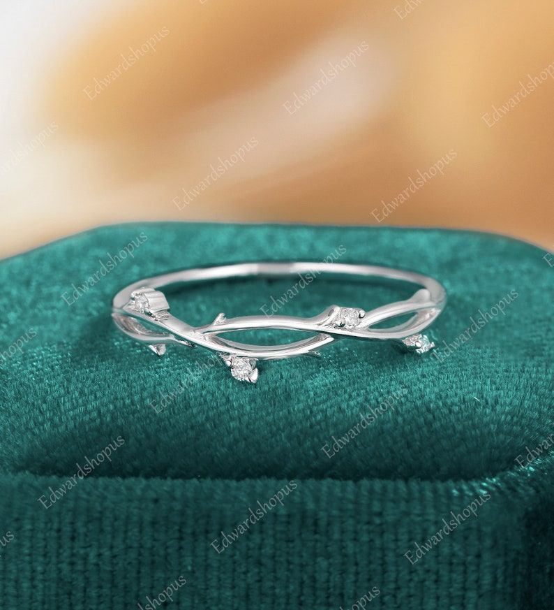 K&ouml;nnte beinhalten: Ein zarter Silberring mit einem Zweigdesign und kleinen klaren Steinen. Der Ring liegt auf einem gr&uuml;nen Samt-Hintergrund.