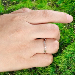 K&ouml;nnte beinhalten: Ein zarter Silberring mit einem Rankendesign und kleinen, klaren Steinen. Der Ring befindet sich an einem Finger und der Hintergrund ist gr&uuml;n.