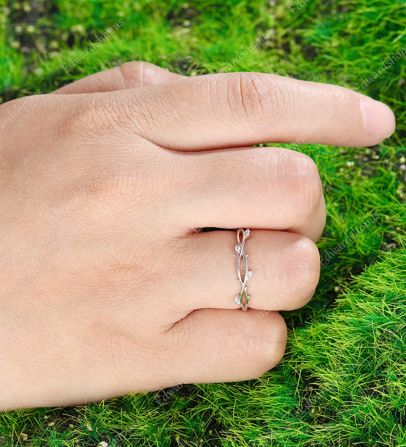 K&ouml;nnte beinhalten: Ein zarter Silberring mit einem Rankendesign und kleinen, klaren Steinen. Der Ring befindet sich an einem Finger und der Hintergrund ist gr&uuml;n.
