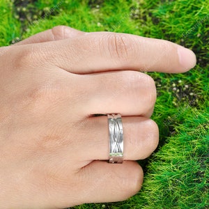 K&ouml;nnte beinhalten: Ein silberner Ring mit einem einzigartigen, komplizierten Design. Der Ring wird am Finger einer Hand getragen, der Hintergrund ist verschwommen.