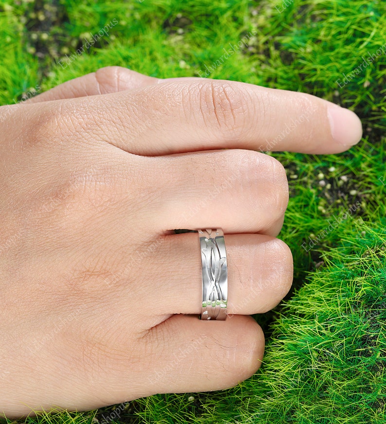 K&ouml;nnte beinhalten: Ein silberner Ring mit einem einzigartigen, komplizierten Design. Der Ring wird am Finger einer Hand getragen, der Hintergrund ist verschwommen.