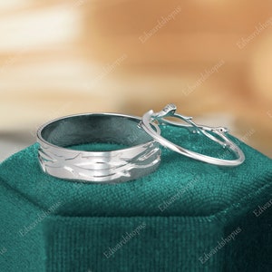 K&ouml;nnte beinhalten: Zwei silberne Eheringe mit einem Baumzweig-Design. Der Ring auf der linken Seite hat eine strukturierte Oberfl&auml;che und der Ring auf der rechten Seite ist ein einfacher Ring mit einem Baumzweig-Design.