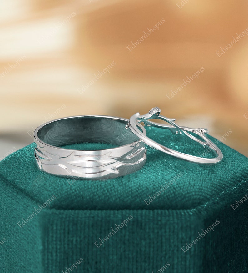 K&ouml;nnte beinhalten: Zwei silberne Eheringe mit einem Baumzweig-Design. Der Ring auf der linken Seite hat eine strukturierte Oberfl&auml;che und der Ring auf der rechten Seite ist ein einfacher Ring mit einem Baumzweig-Design.