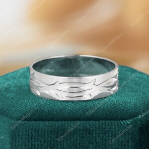 K&ouml;nnte beinhalten: Ein silberner Bandring mit einem detaillierten Design aus ineinander verschlungenen &Auml;sten. Der Ring wird auf einem gr&uuml;nen Samtstoff pr&auml;sentiert.