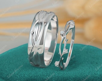 Könnte beinhalten: Ein Paar Eheringe mit einem Rankendesign. Der Ring links hat eine glatte, polierte Oberfläche, während der Ring rechts ein filigraneres Design mit kleinen Diamanten aufweist.