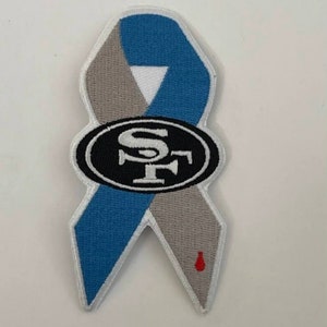 May include: A blue and gray ribbon with a white "SF" logo in a black oval. A small red drop is on the bottom of the ribbon.