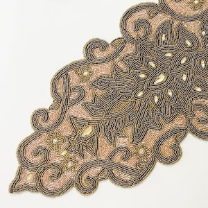 Puede incluir: Un camino de mesa de cuentas con un diseño floral en tonos marrones y beige. El camino de mesa tiene un borde festoneado y está hecho de pequeñas cuentas.