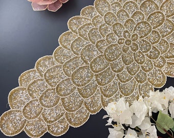 Puede incluir: Un camino de mesa de cuentas doradas y blancas con un diseño floral. El camino de mesa está hecho de pequeñas cuentas redondas que están cosidas juntas para crear un patrón delicado e intrincado.