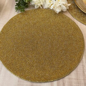 May include: A round, gold beaded placemat with a swirling pattern. The placemat is made of small, gold beads that are woven together to create a unique and elegant design.
