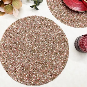 May include: Two round pink and gold beaded placemats with white pearl accents. The placemats are on a white surface.