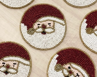 May include: Set of six round beaded coasters featuring a Santa Claus design. The coasters are white with red and gold accents.