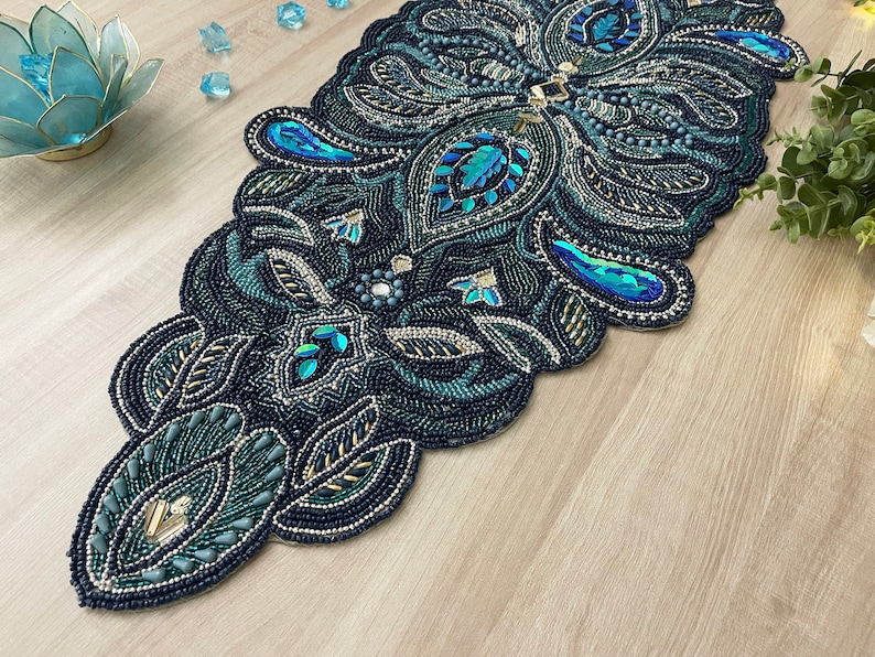 Puede incluir: Un camino de mesa de cuentas color verde azulado y dorado con un dise&ntilde;o de paisley. El camino de mesa est&aacute; hecho de cuentas peque&ntilde;as y tiene un acabado brillante e iridiscente.