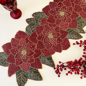 May include: A red and green beaded table runner featuring a poinsettia design. The runner is crafted from small beads and has a festive Christmas theme.