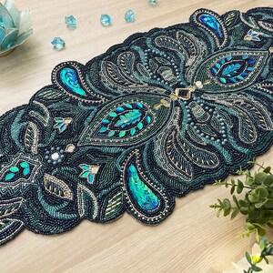 Puede incluir: Un camino de mesa de cuentas color verde azulado y dorado con un dise&ntilde;o de paisley. El camino de mesa est&aacute; hecho de peque&ntilde;as cuentas y lentejuelas y tiene un borde festoneado.
