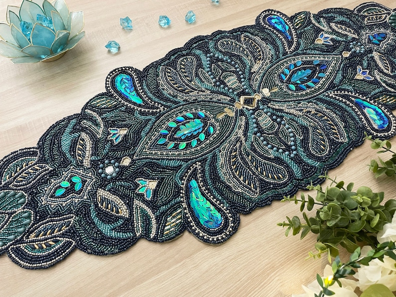 Puede incluir: Un camino de mesa de cuentas color verde azulado y dorado con un dise&ntilde;o de paisley. El camino de mesa est&aacute; hecho de peque&ntilde;as cuentas y lentejuelas y tiene un borde festoneado.