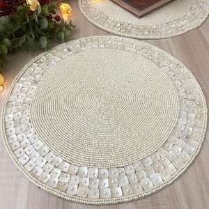 May include: A round white beaded placemat with a decorative border of white shell pieces.