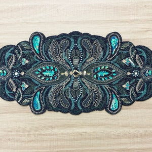 Puede incluir: Un camino de mesa negro y turquesa con cuentas con un dise&ntilde;o de paisley. El camino de mesa est&aacute; decorado con lentejuelas y cuentas en un patr&oacute;n floral.