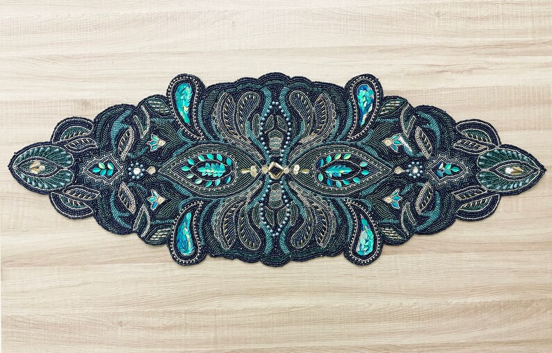 Puede incluir: Un camino de mesa negro y turquesa con cuentas con un dise&ntilde;o de paisley. El camino de mesa est&aacute; decorado con lentejuelas y cuentas en un patr&oacute;n floral.