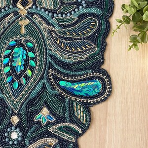 Puede incluir: Un camino de mesa de cuentas con un dise&ntilde;o de paisley en tonos de verde, azul y dorado. El camino de mesa est&aacute; hecho de peque&ntilde;as cuentas y lentejuelas, creando un patr&oacute;n texturizado e intrincado.