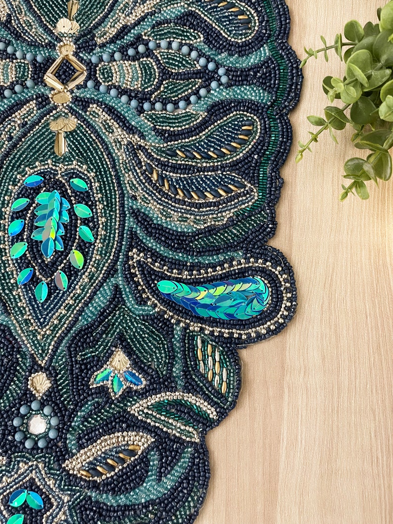 Puede incluir: Un camino de mesa de cuentas con un dise&ntilde;o de paisley en tonos de verde, azul y dorado. El camino de mesa est&aacute; hecho de peque&ntilde;as cuentas y lentejuelas, creando un patr&oacute;n texturizado e intrincado.