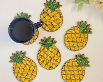 May include: Six yellow and green pineapple-shaped coasters made of beads. The coasters are arranged in a circle on a white surface.