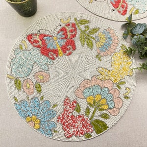 Peut inclure: Nappe ronde perlée avec un motif floral et papillon. Le napperon présente un fond clair avec des perles colorées formant des fleurs, des papillons et un lapin. Le motif comprend des accents rouges, bleus, jaunes et verts.